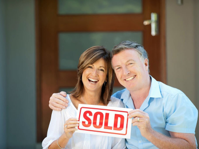 Happy mature couple holding sold sign in front of a new house