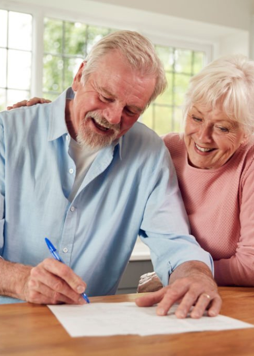 Retired Senior Couple Sitting In Kitchen At Home Signing Financial Document